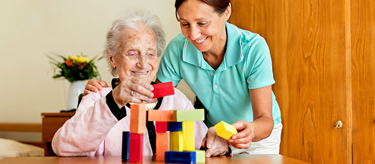 Dementia and Occupational Therapy - Home caregiver and senior adult woman playing with blocks